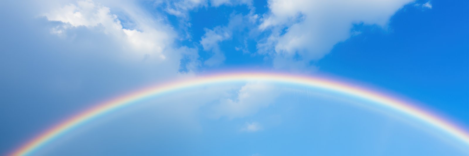 A stunning rainbow spans the horizon, its vivid colors contrasting beautifully with the clear blue sky and scattered white clouds